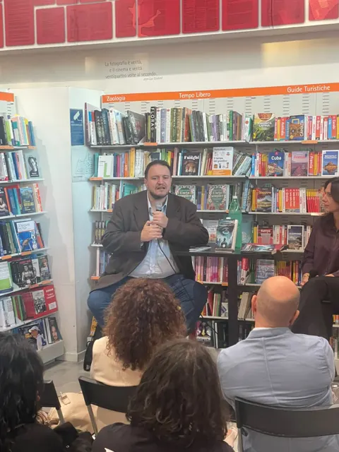 Rosario Di Leva parla al microfono durante la presentazione alla Feltrinelli di Napoli Stazione Centrale, con il pubblico in primo piano