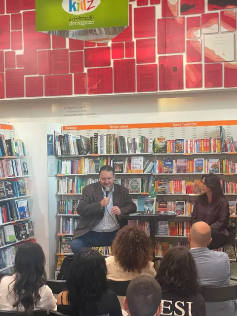 Rosario Di Leva e la giornalista Anna Chiara De Rosa davanti agli scaffali della Feltrinelli, con il pubblico seduto