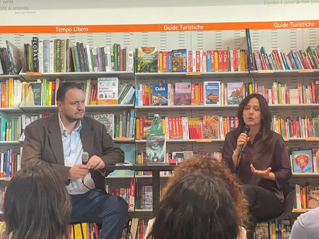 Rosario Di Leva e Anna Chiara De Rosa seduti tra gli scaffali della Feltrinelli, lei parla al microfono